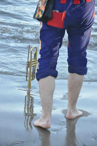 Ein Trompeter steht Barfuss auf nassem Sand